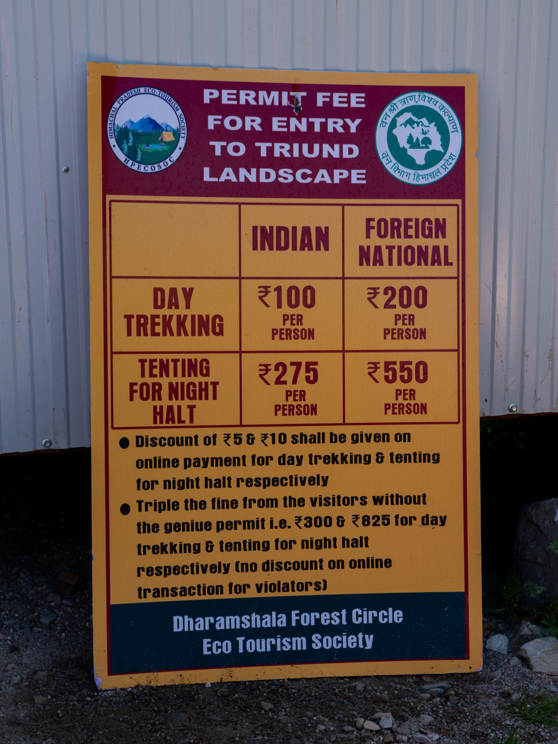 The price board next to the entry checkpoint near Gallu Temple, Dharamshala showing the costs for Indians and foreigners for overnight or day treks for Triund Trek