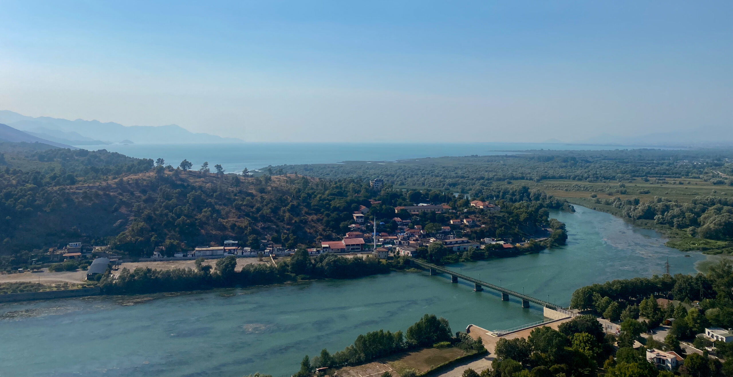 A view of the bright blue river that leads in Shkodra Lake in the distance surrounded by lakeside villages from Shkodra Castle