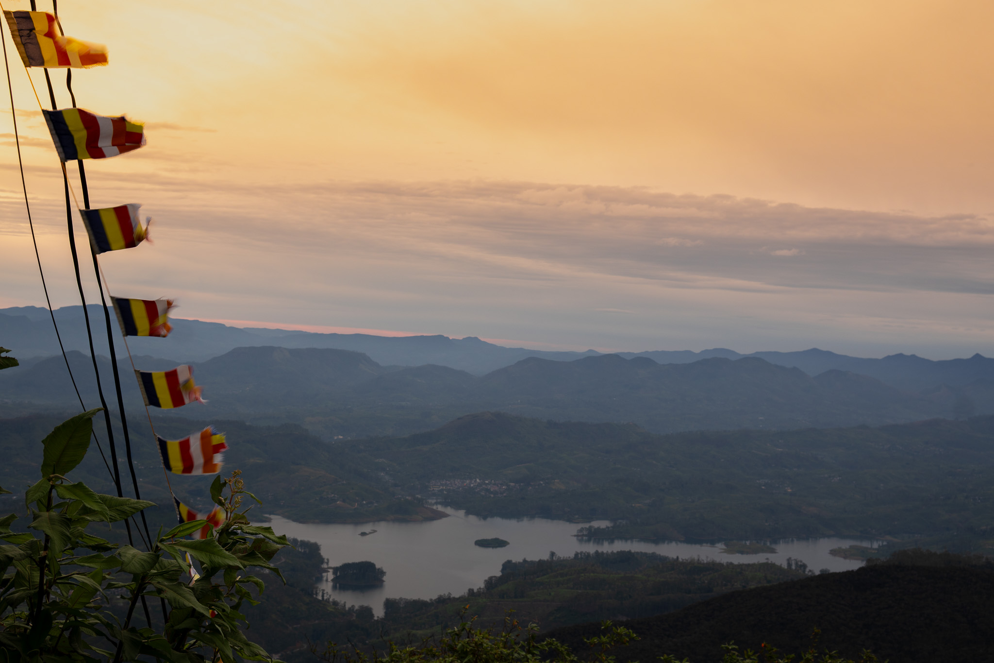 Sunrise view from Adam's Peak (Sri Pada) Sri Lanka with Buddhist prayer flags over misty mountain valleys and reservoir.