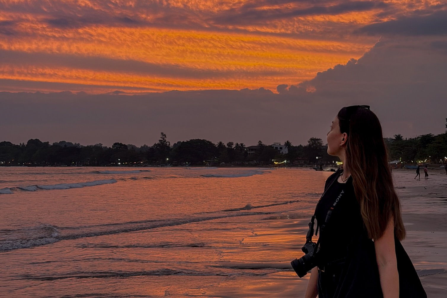 A women stood on a beach on the south coast of Sri Lanka with an orange sunset lighting the sky