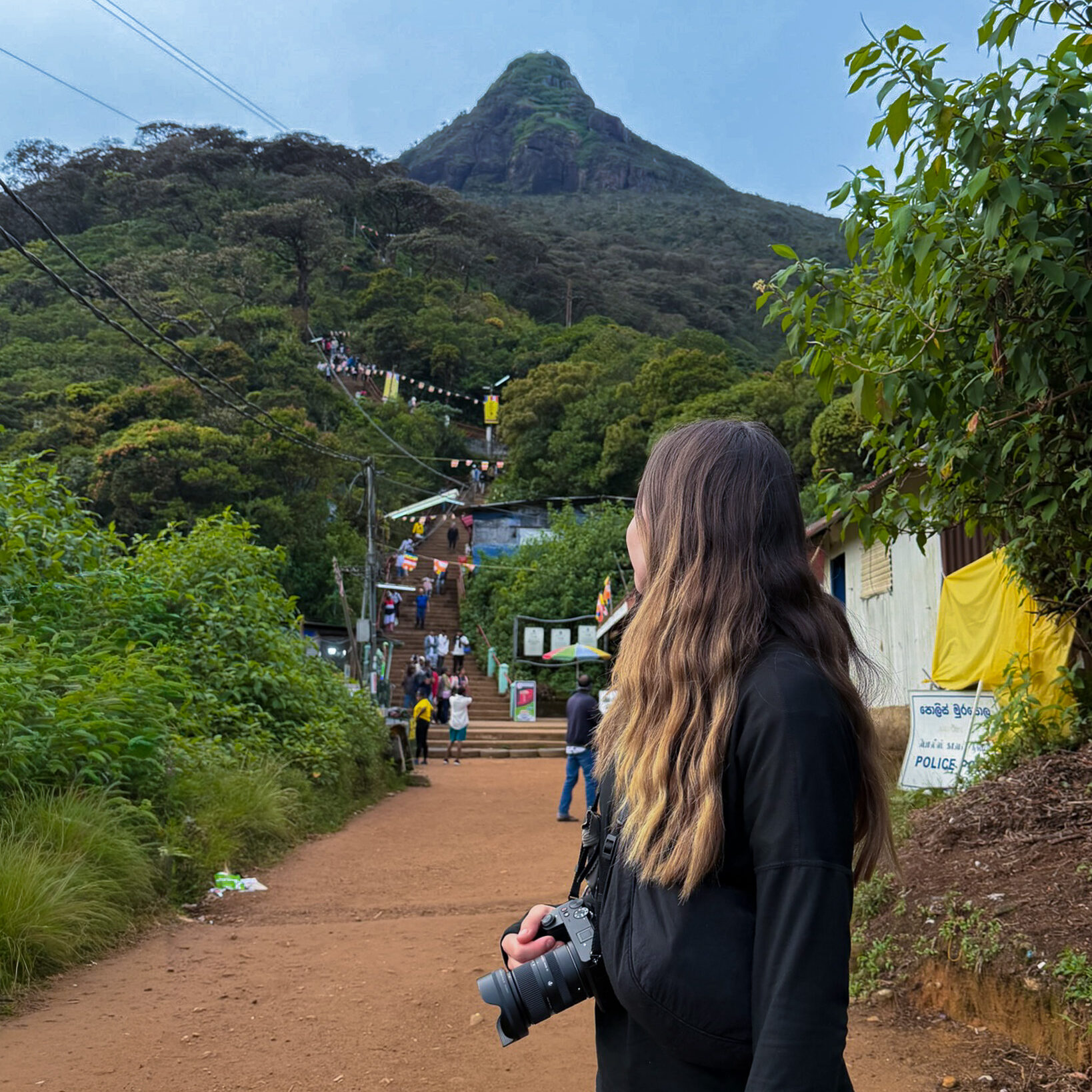 A women stood on a flat stretch of ground looking up at Adam's Peak (Sri Pada) in Sri Lanka, after a morning climb.