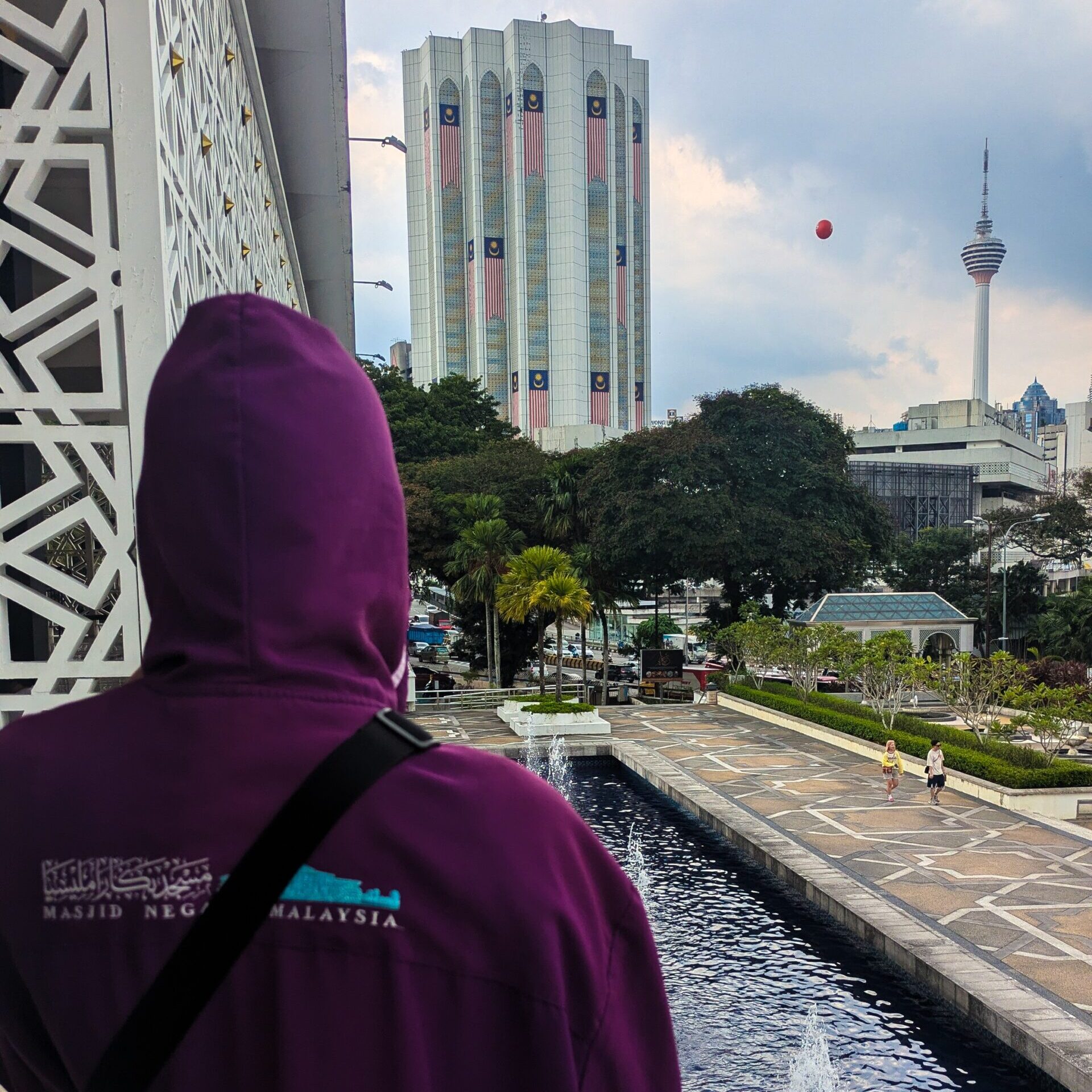 A gowned individual outside of the national mosque in Kuala Lumpur, Malaysia with skyscrapers in the background