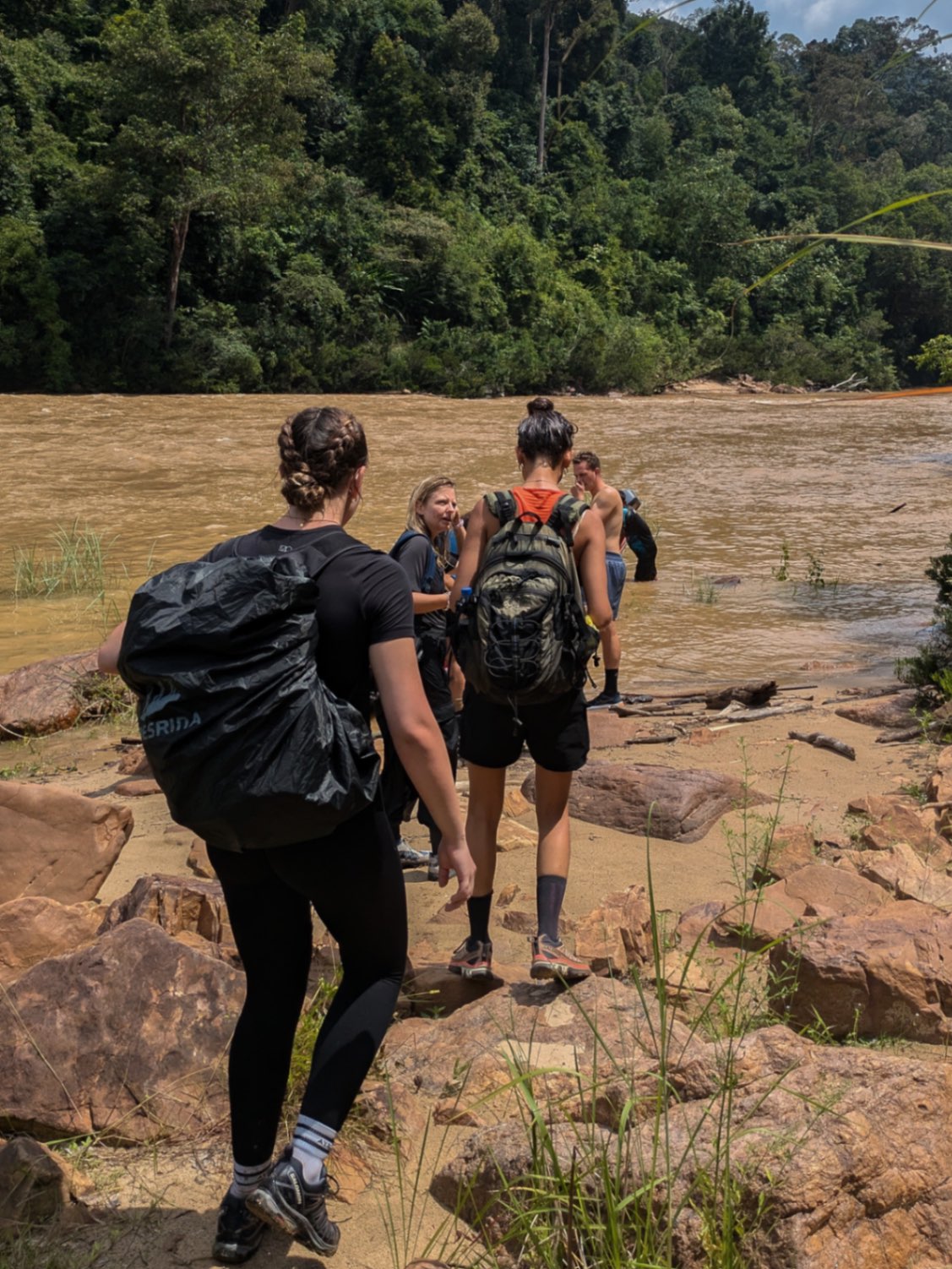 People with backpacks walking near a jungle river, during a hot day