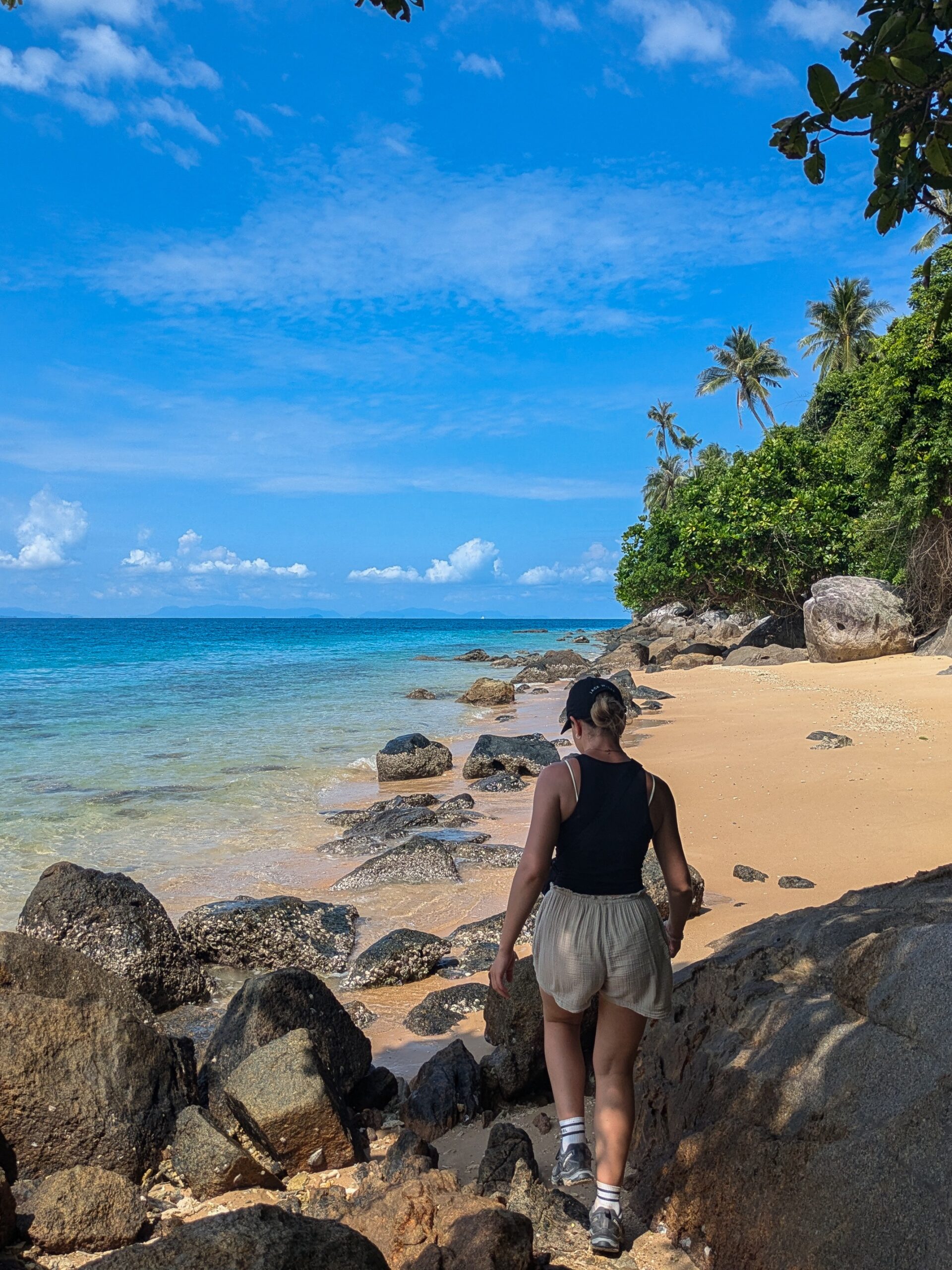 A woman walking over some rocks along a secluded beach with stunning waters and a clear sky in Perhentian Islands, Malaysia