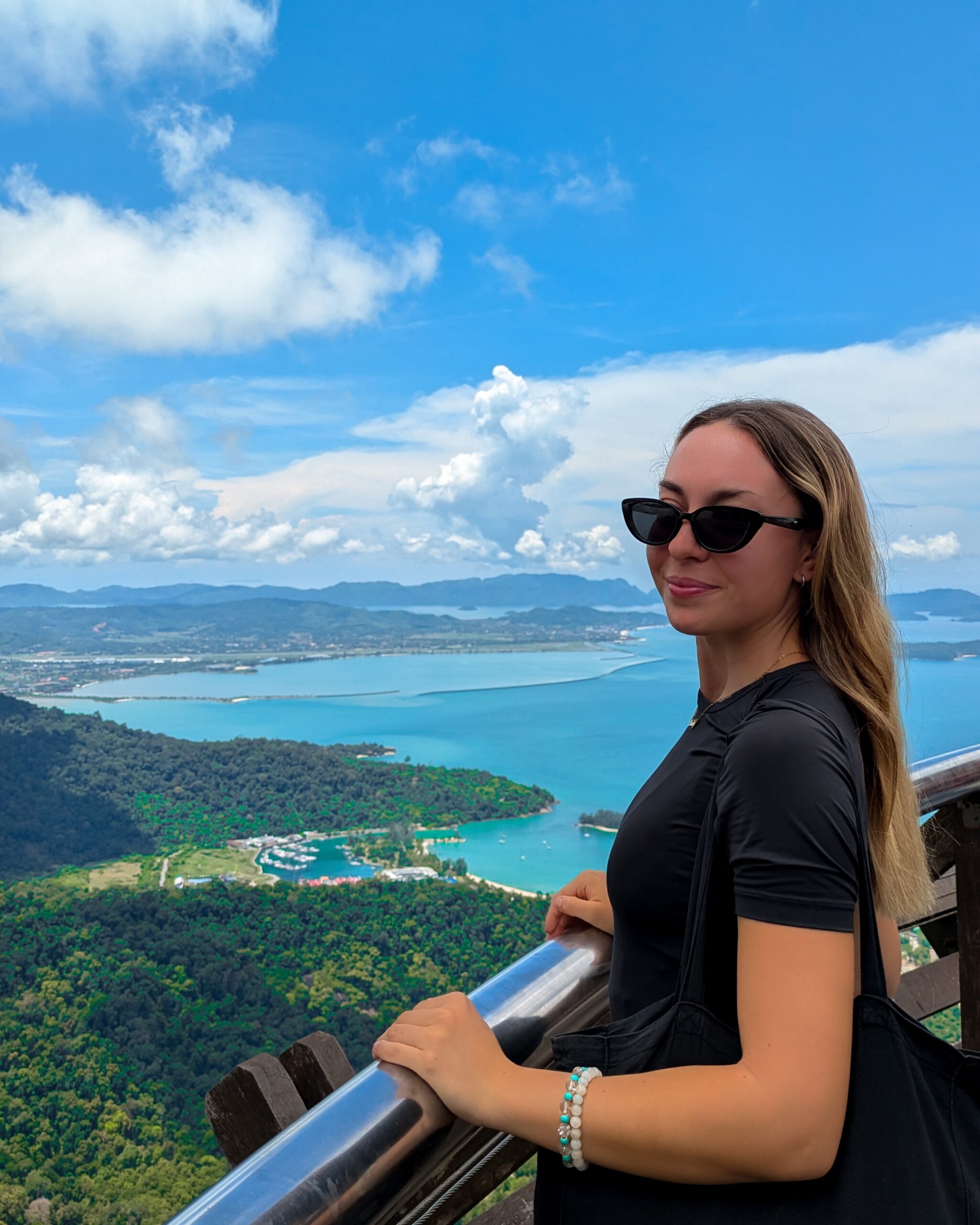 A woman at a scenic mountain overlook with a sweeping background view of tropical islands and turquoise coastal waters of Langkawi, Malaysia.