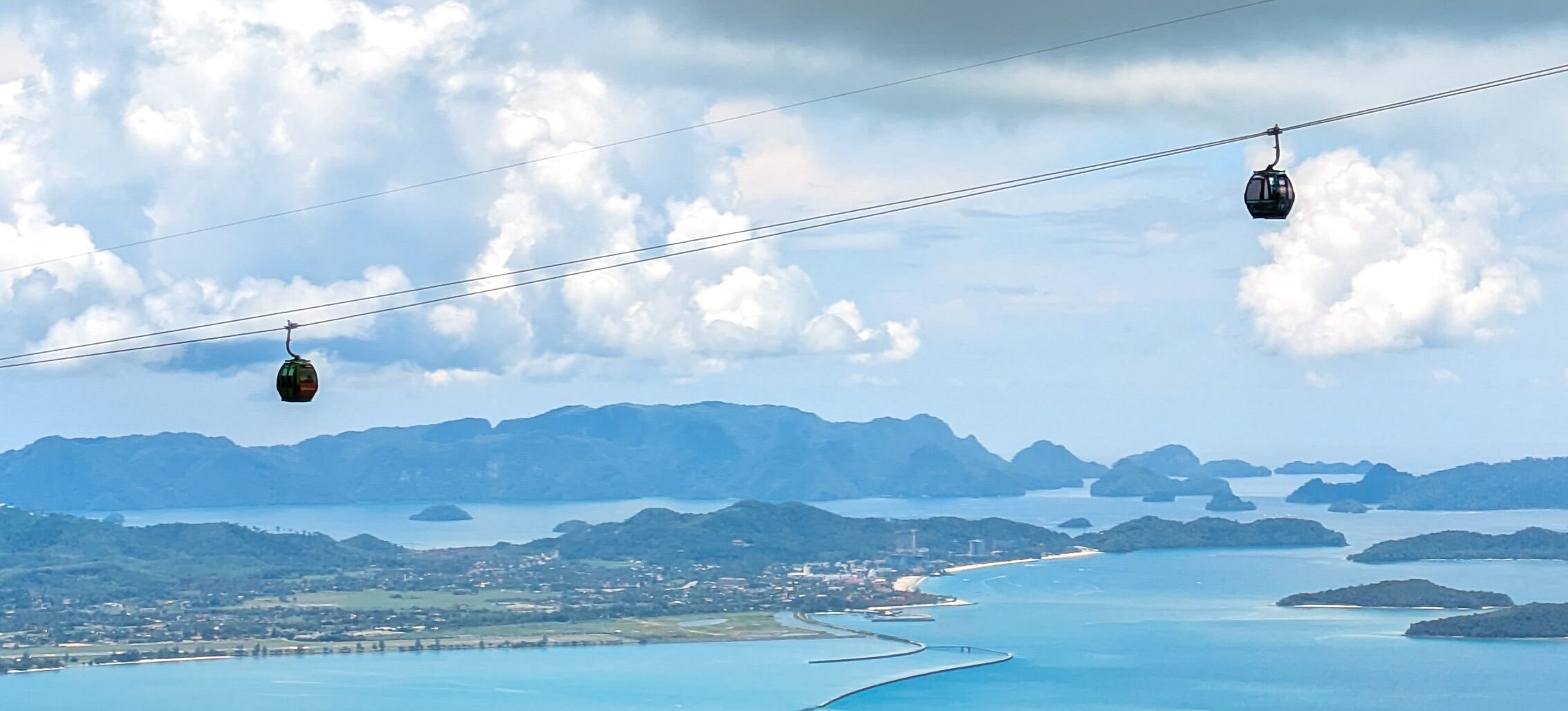 Two cable cars suspended in the air with a panoramic backdrop of tropical islands and a blue ocean of Langkawi, Malaysia
