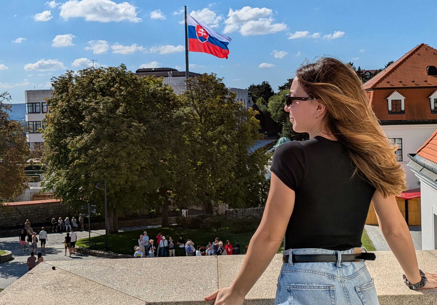 A women stood on a concrete balcony area with a Slovakian flag flying in the city of Bratislava.