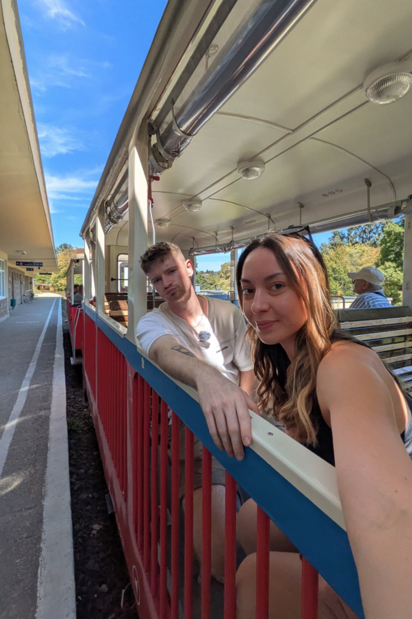 2 people sat on a train with no windows, a blue sky