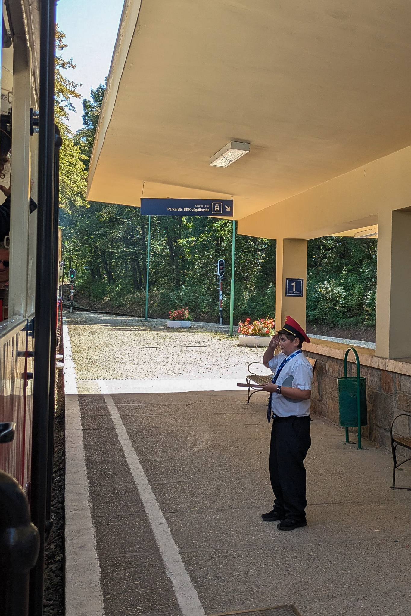 A young boy dressed in a train conductors outfit, saluting the train driver on the platform of a train station