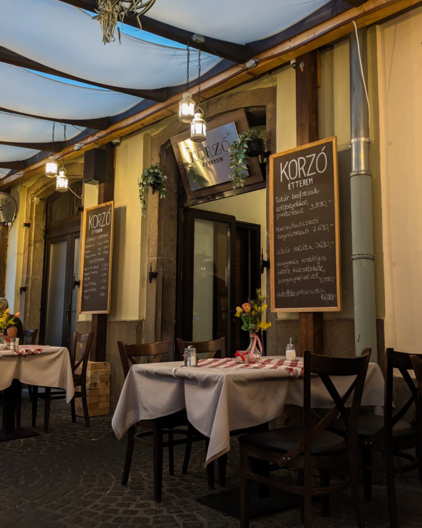 A typical Hungarian restaurant at night with warm lighting and classic white and red checkered table clothes.