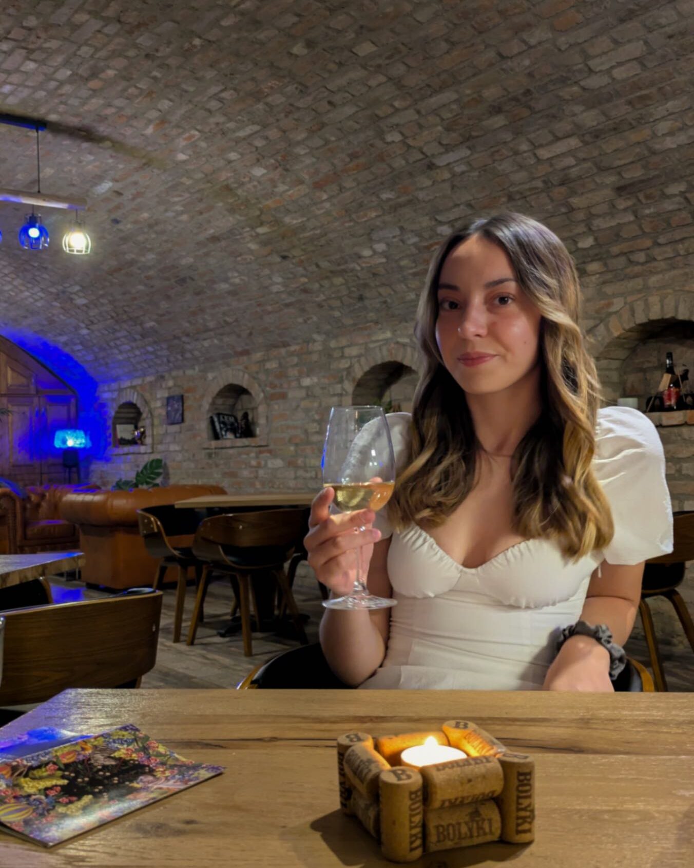 A women with a glass of wine inside of a cave cellar with a candle lit