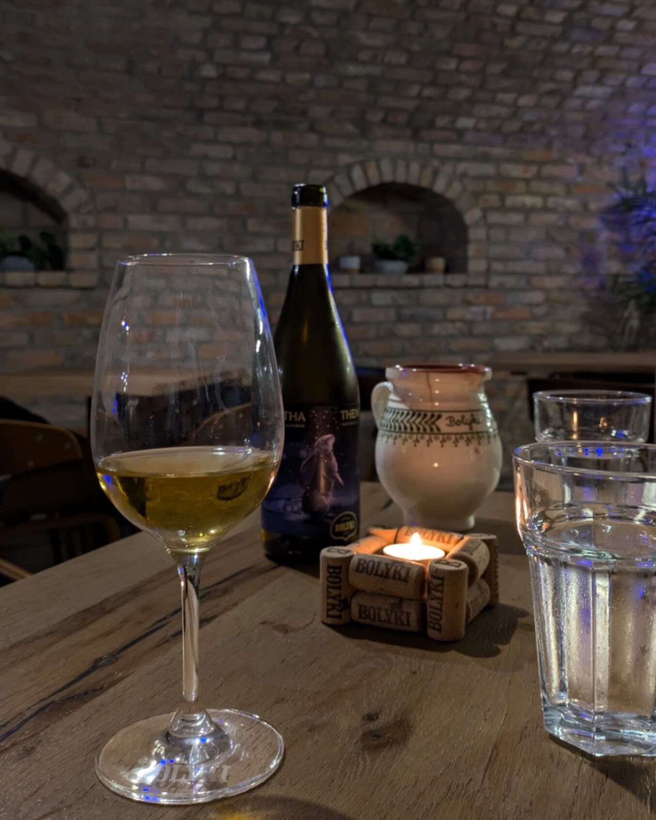 A cozy environment. A glass of wine sat on a table with a bottle of wine and glass of water on the table with a candle