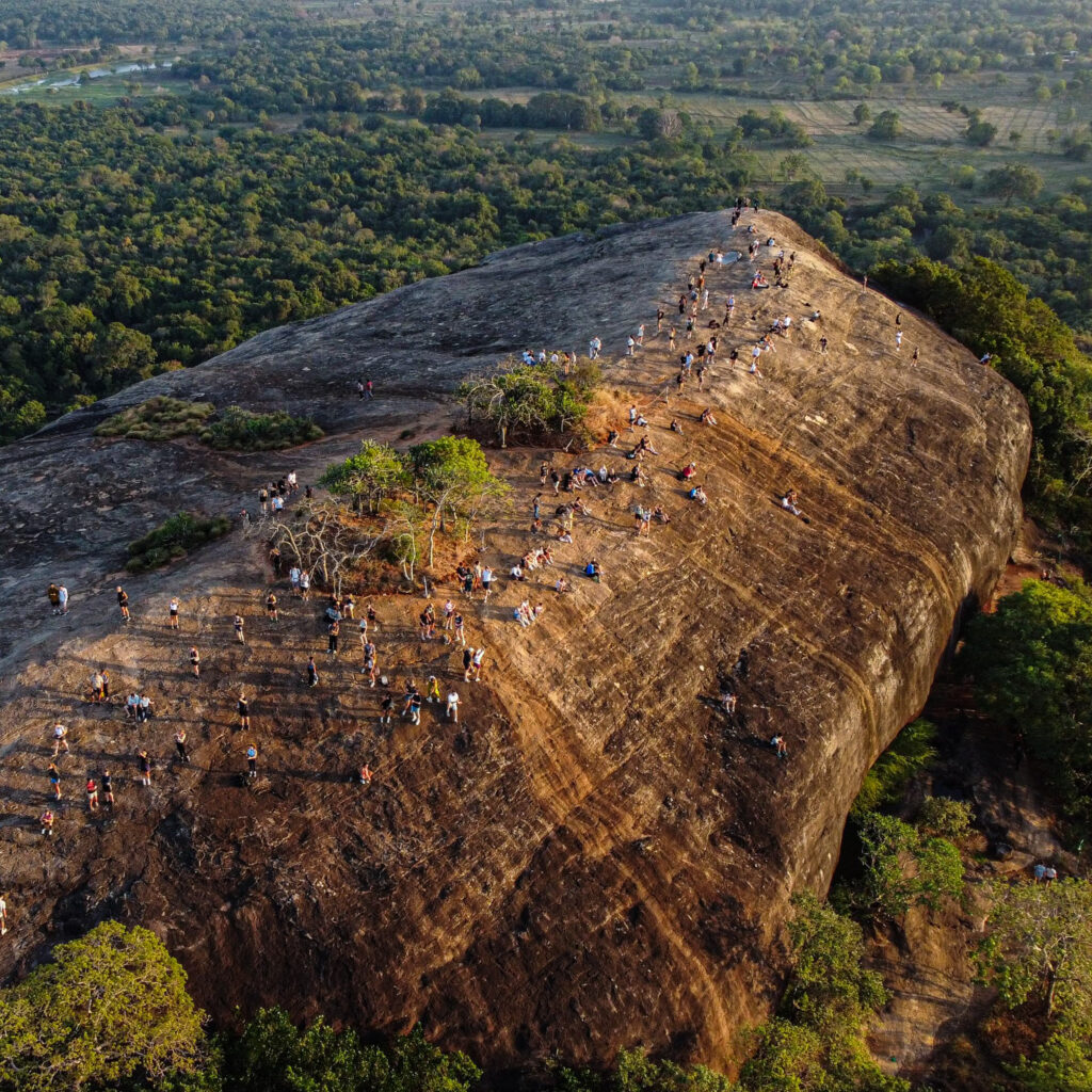 An aerial shot of Pidurangala Rock during a beautiful light. The jungle floor is green and bright and Sigiriya is in the distance.