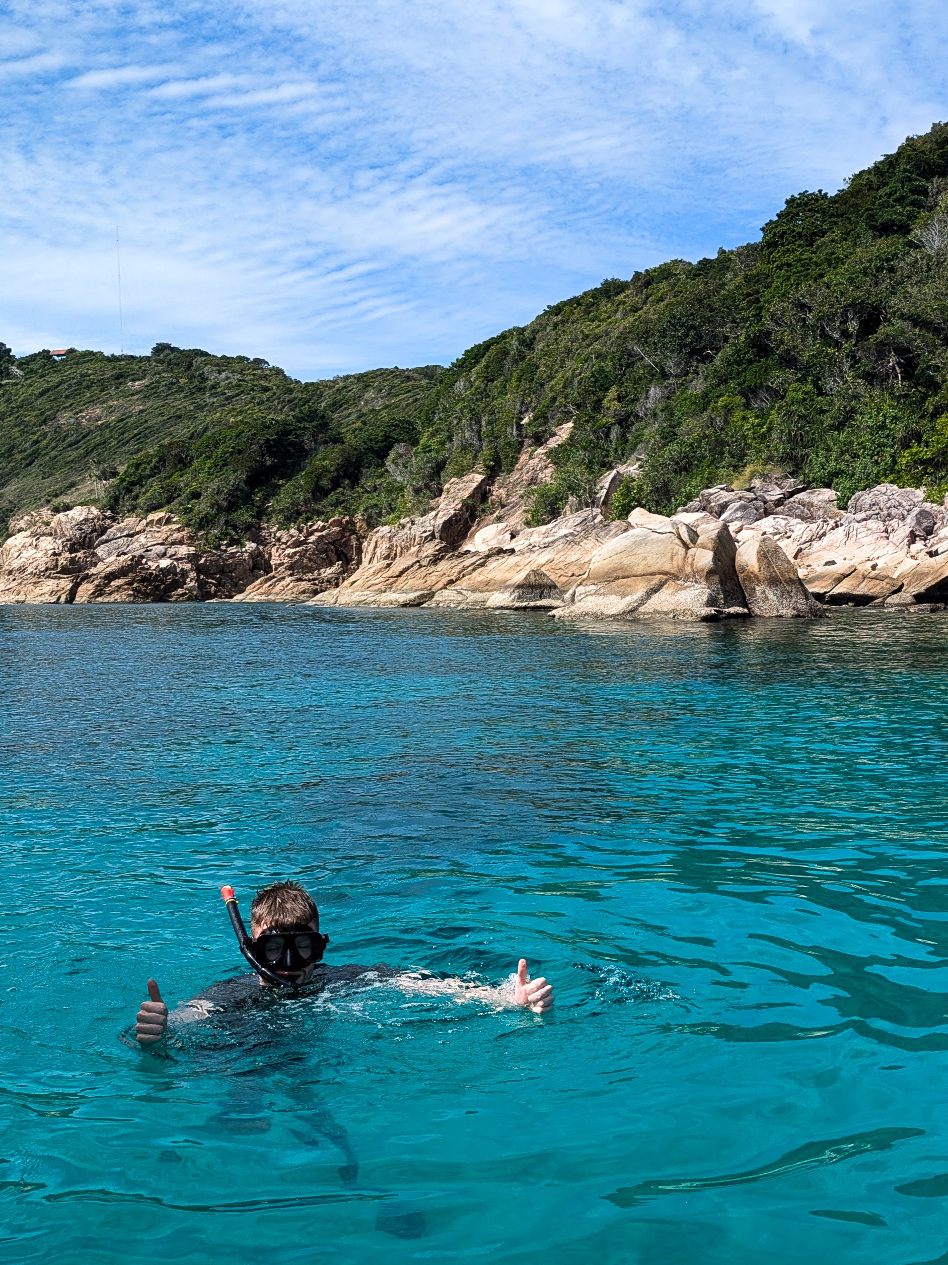 someone snorkelling in blue waters with an island in the background