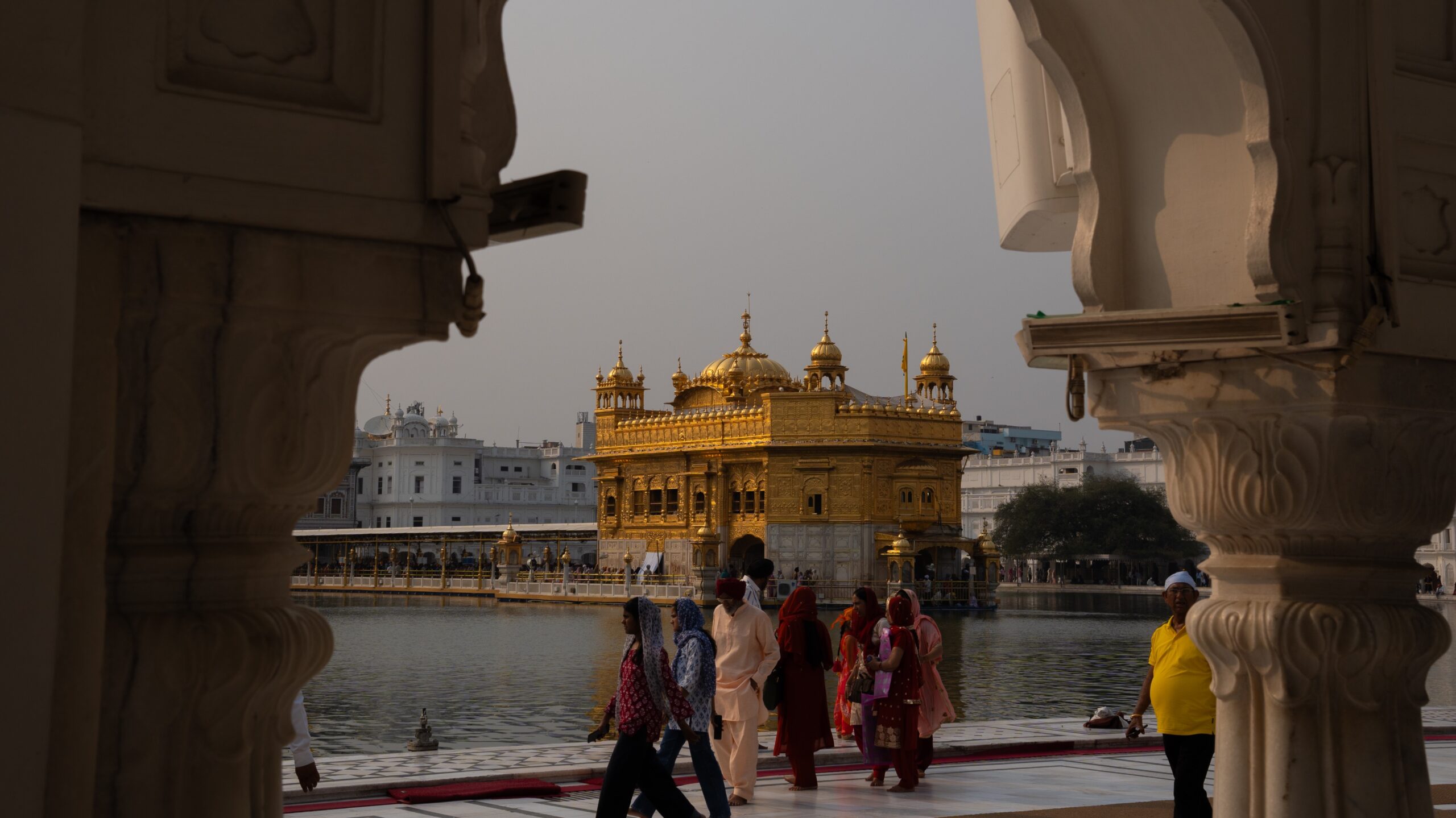 The Golden Temple Temple of Amritsar through an archway with Sikh people walking around the walkway