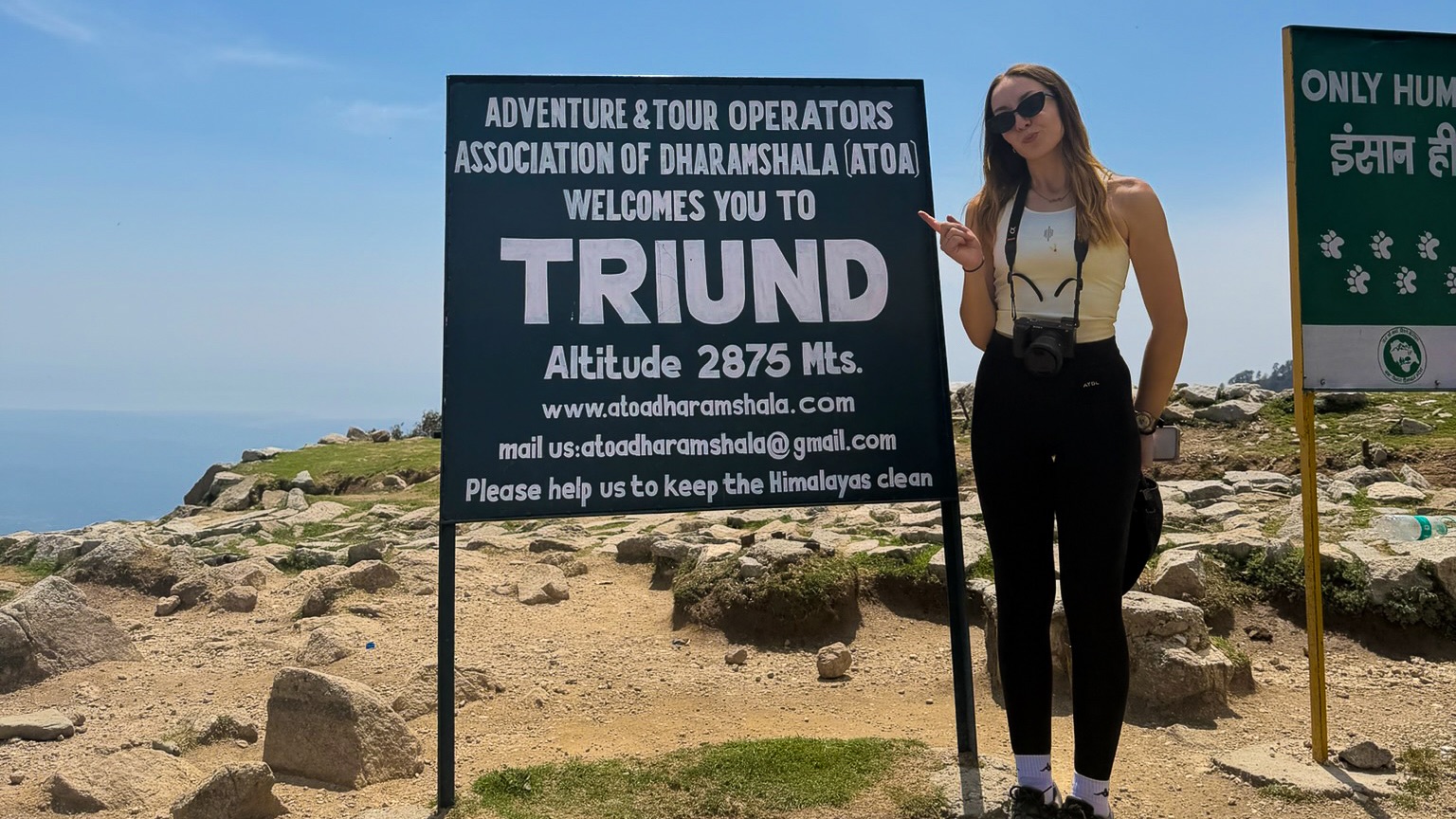 A women stood next to the sign for the Triund Trek in Dharamshala, a popular thing to do in the area