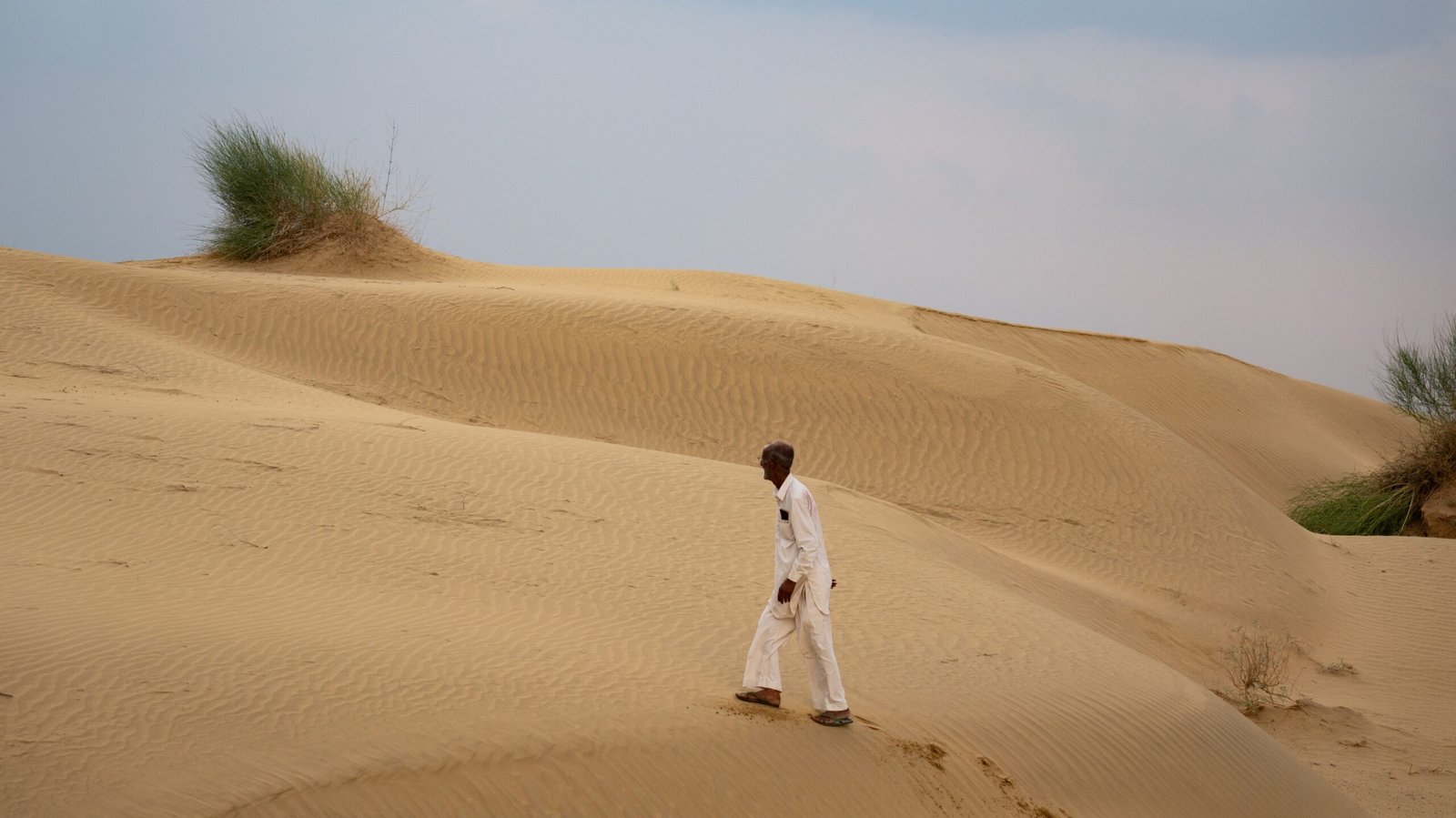 An elderly man walking across untouched sand in the Thar Desert