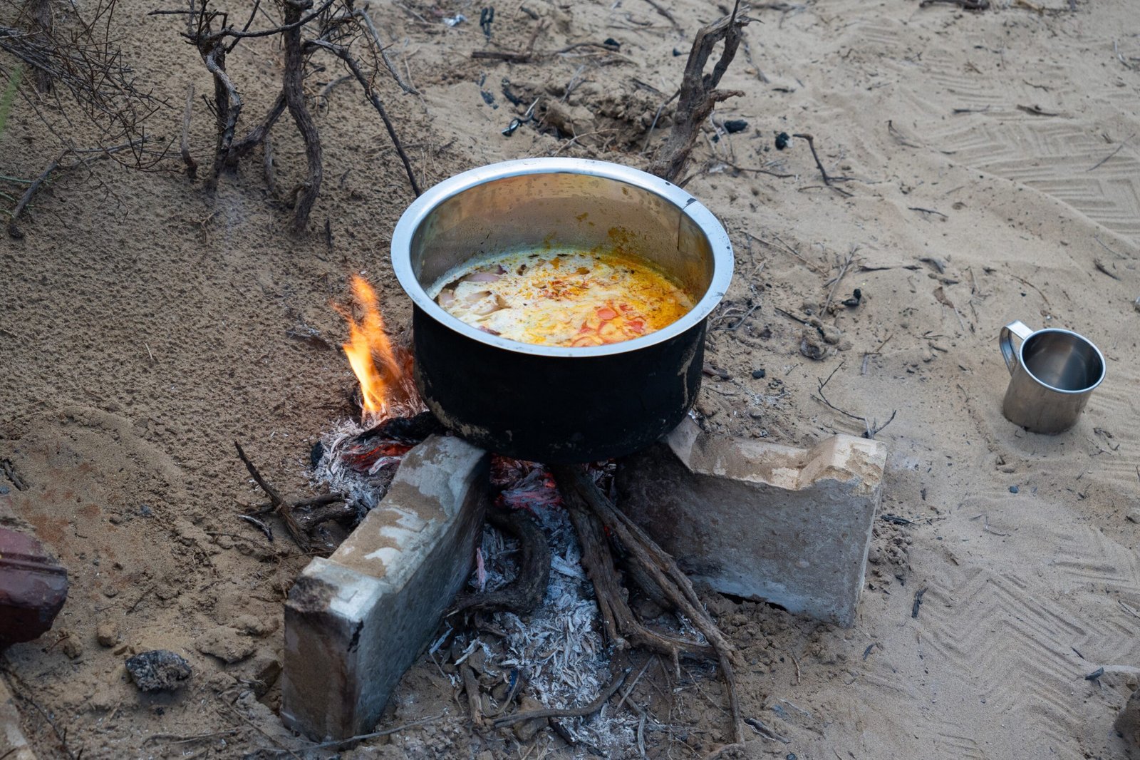 A pot bubbling a food over an open fire in the desert