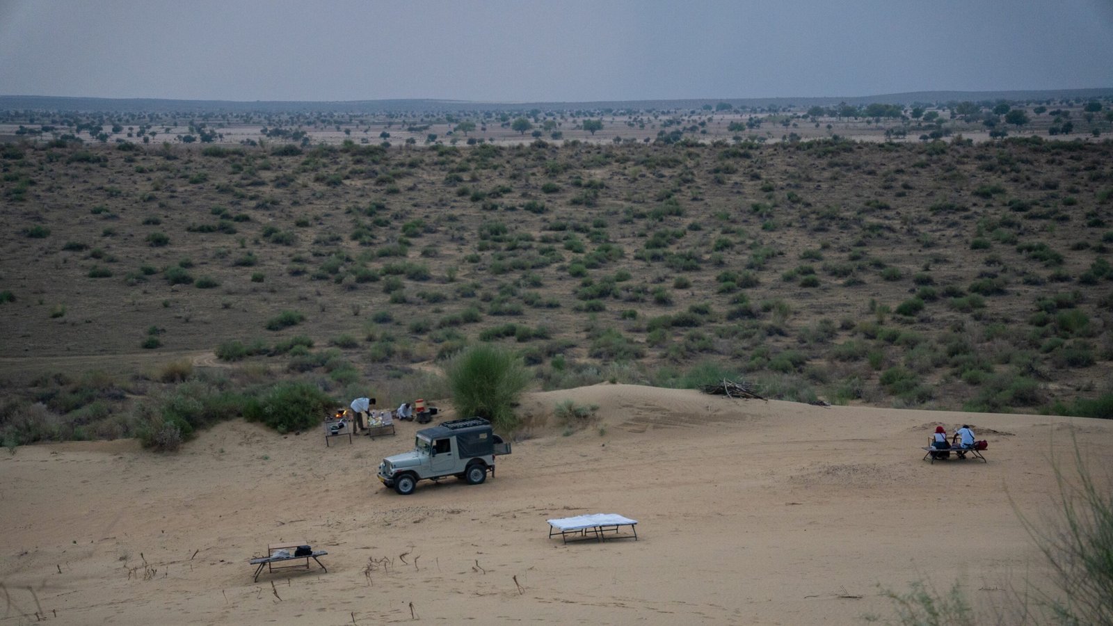 An overview of a desert stay in the Thar desert set up with a jeep, open fire and beds