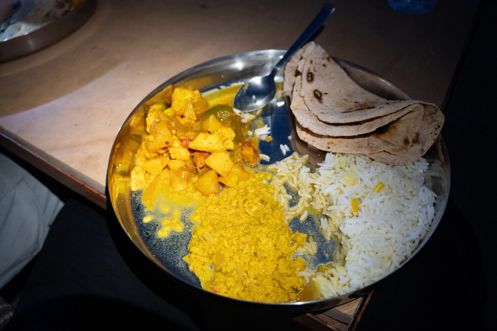 A plate of food served in a metal tray, including dal, potatoes, rice and chapatis