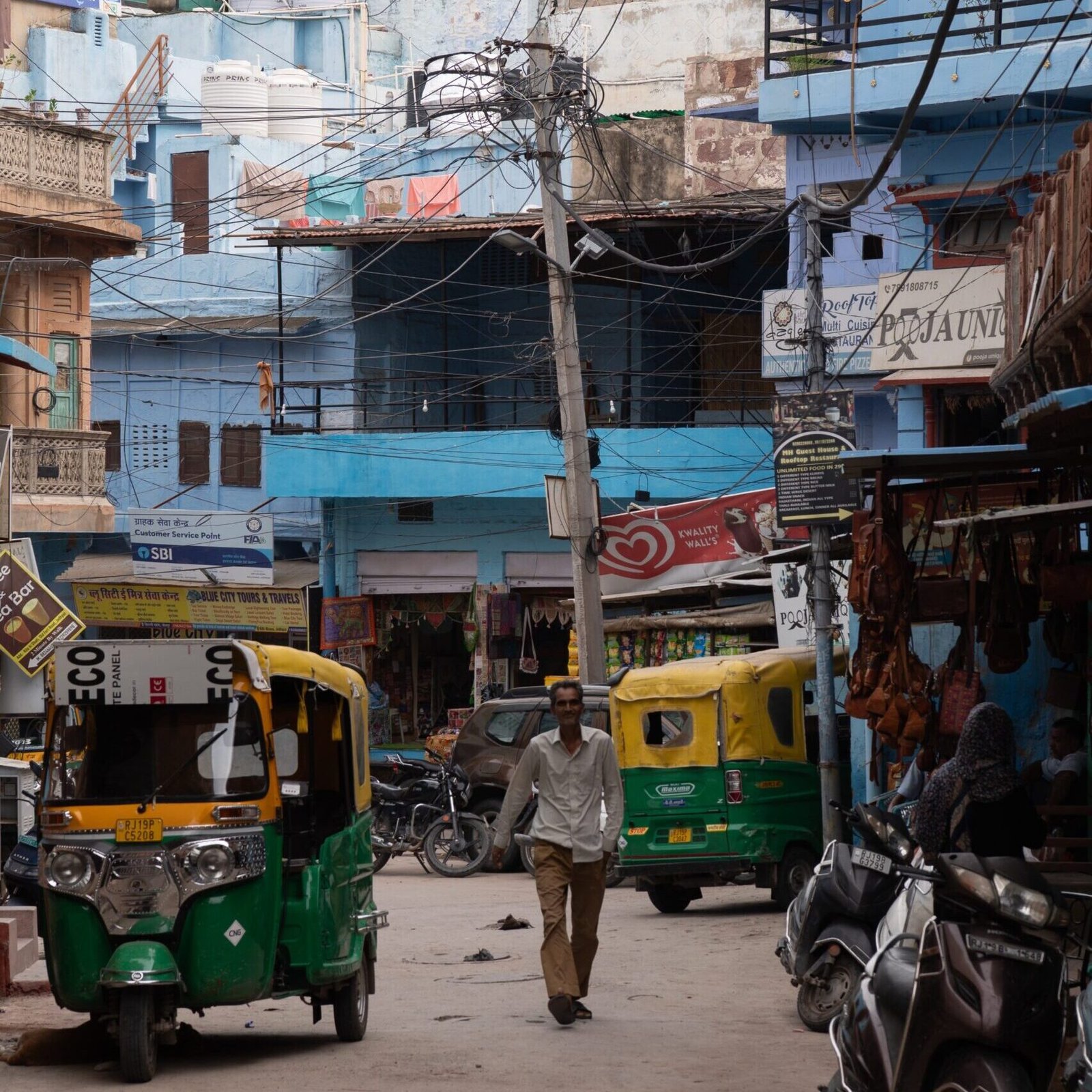 A chaotic street with auto-rickshaws, people and wires