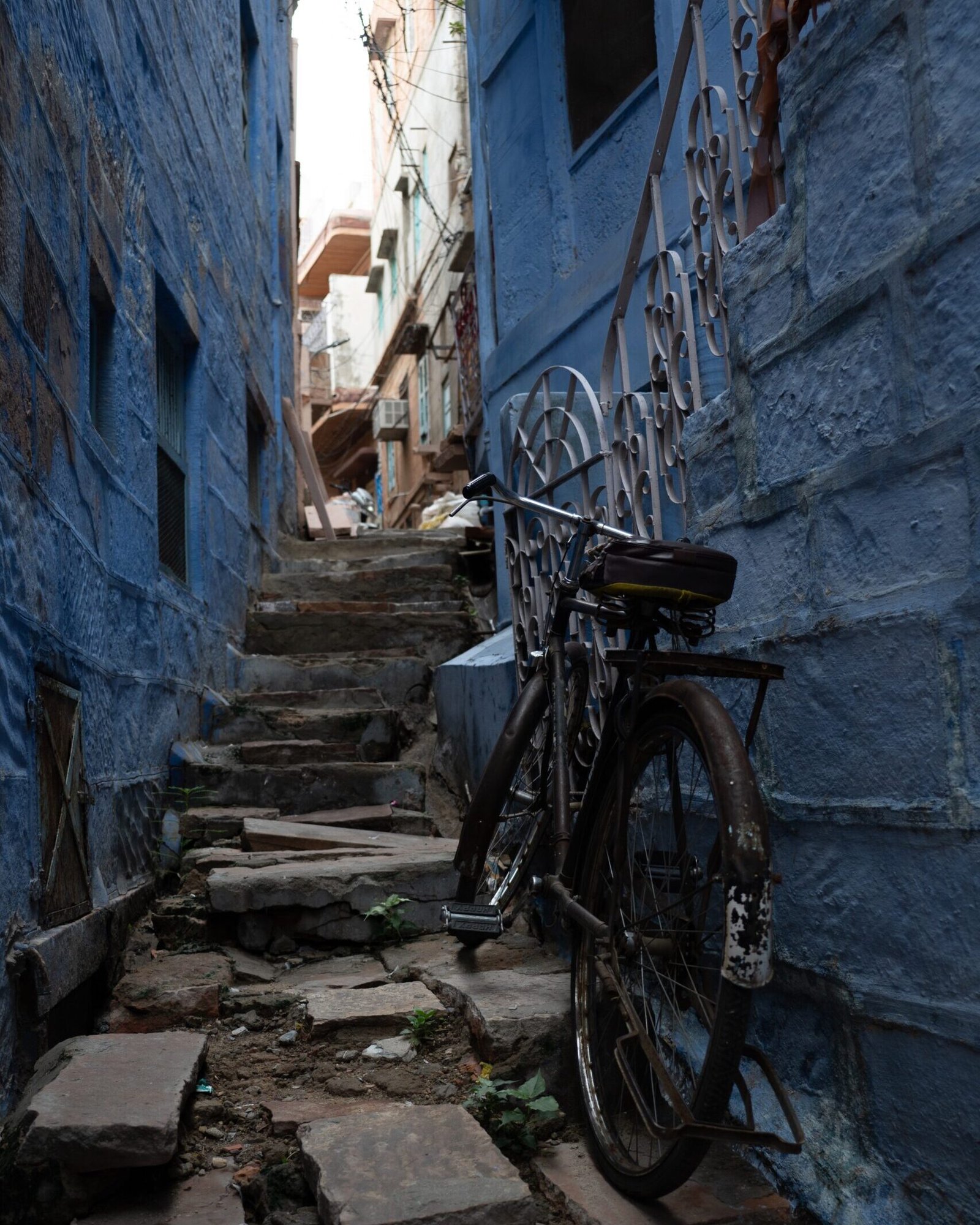 An old bike parked on a set of stairs leading up through blue buildings in the Blue City, Jodhpur