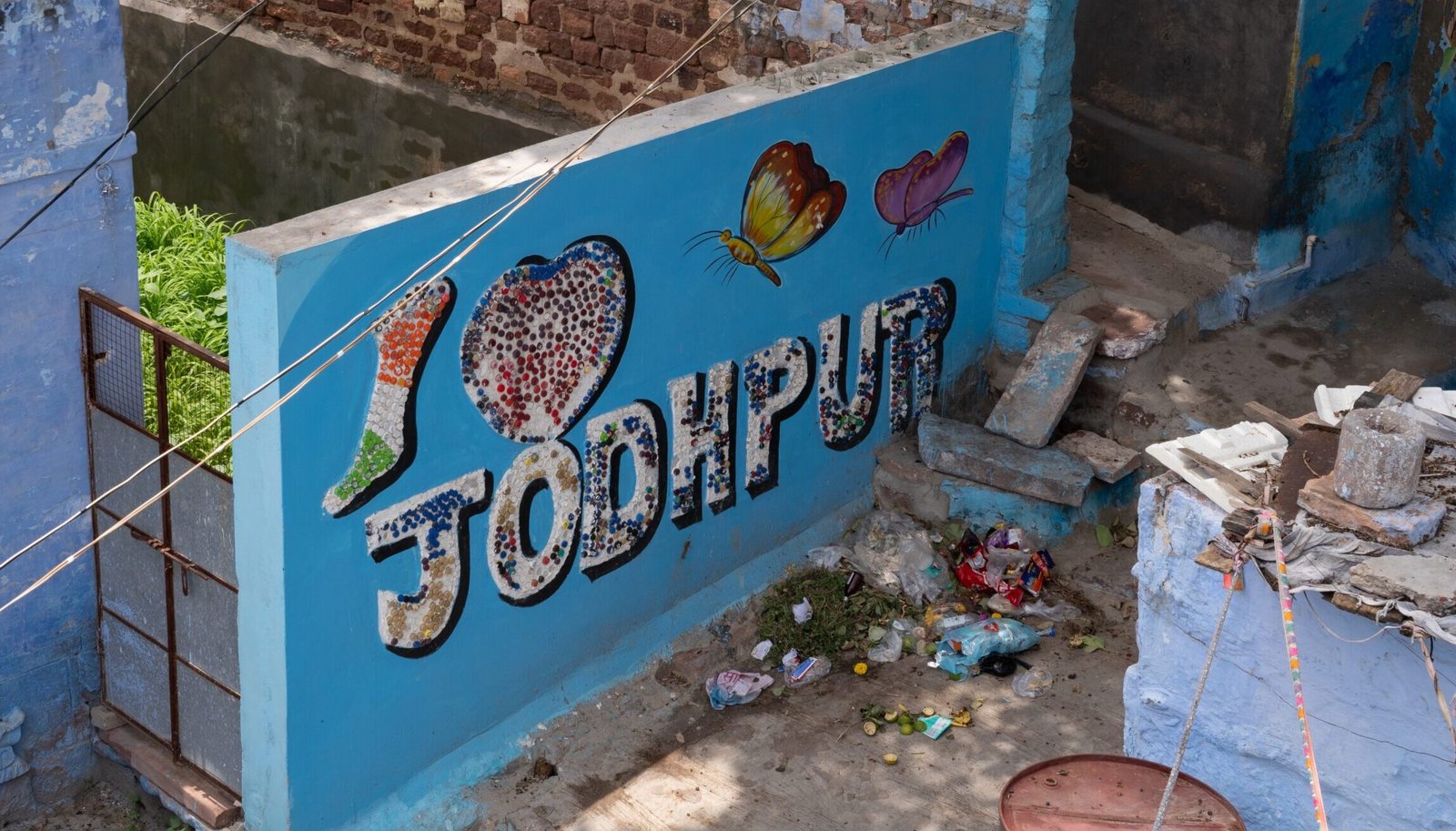 A sign that reads "I love Jodhpur" with a lot of trash around the base of the wall