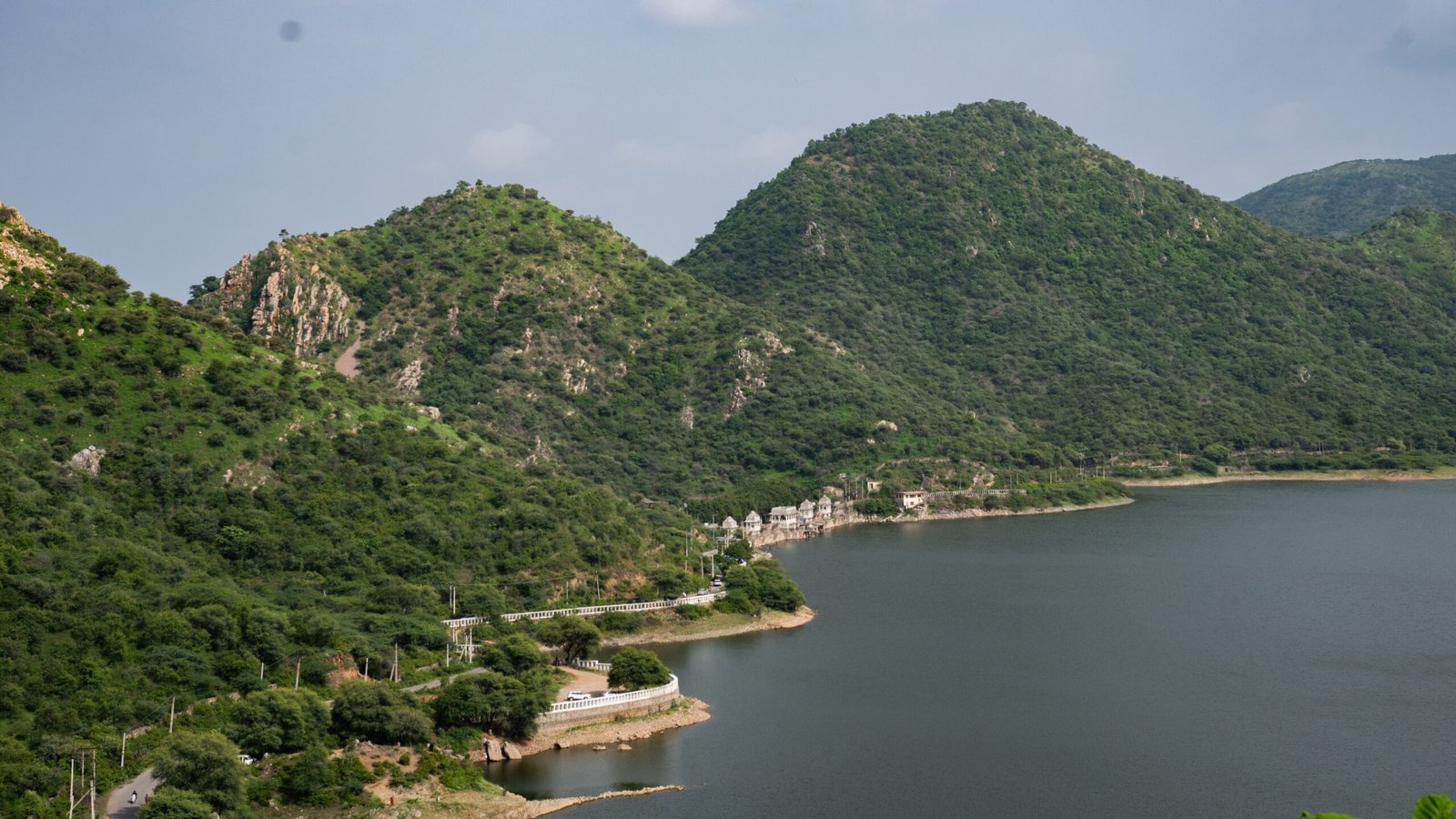 The edge of a lake, with white marble architecture around it, next to a road.