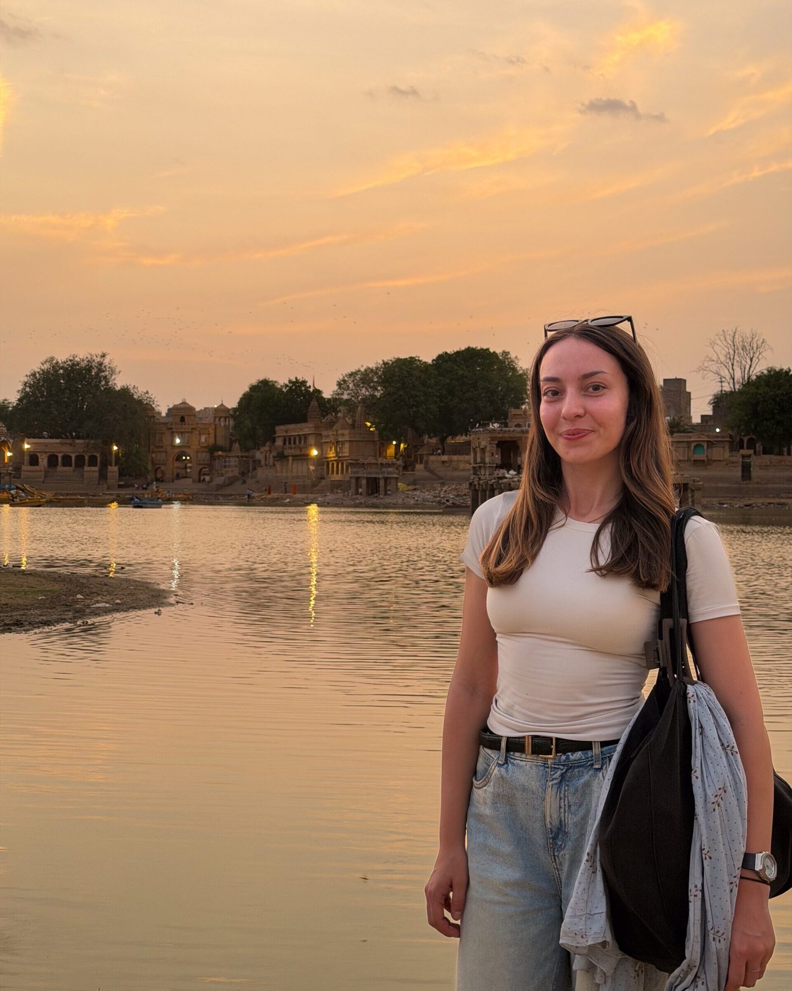 A women stood at a lake with the sun setting behind her