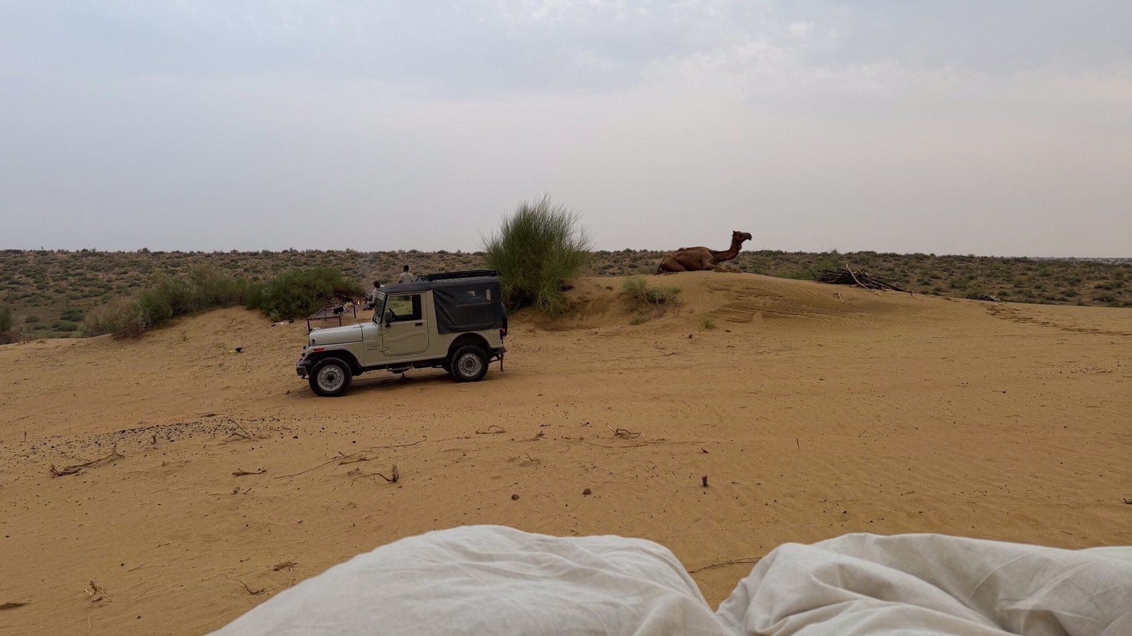 A dramatic desert landscape from a bed, featuring a camel and jeep