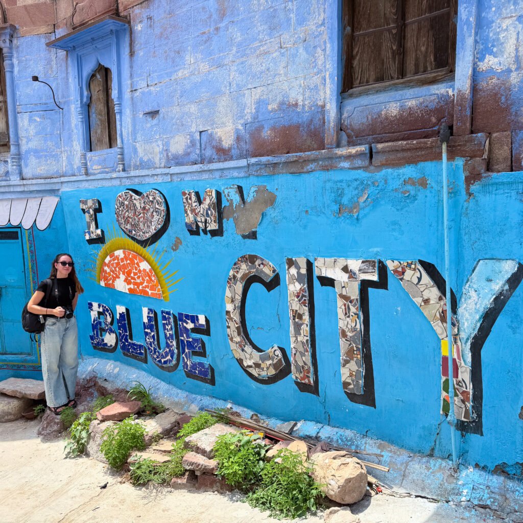 A women stood next to a blue wall that reads "I love my Blue City" in Jodhpur, India