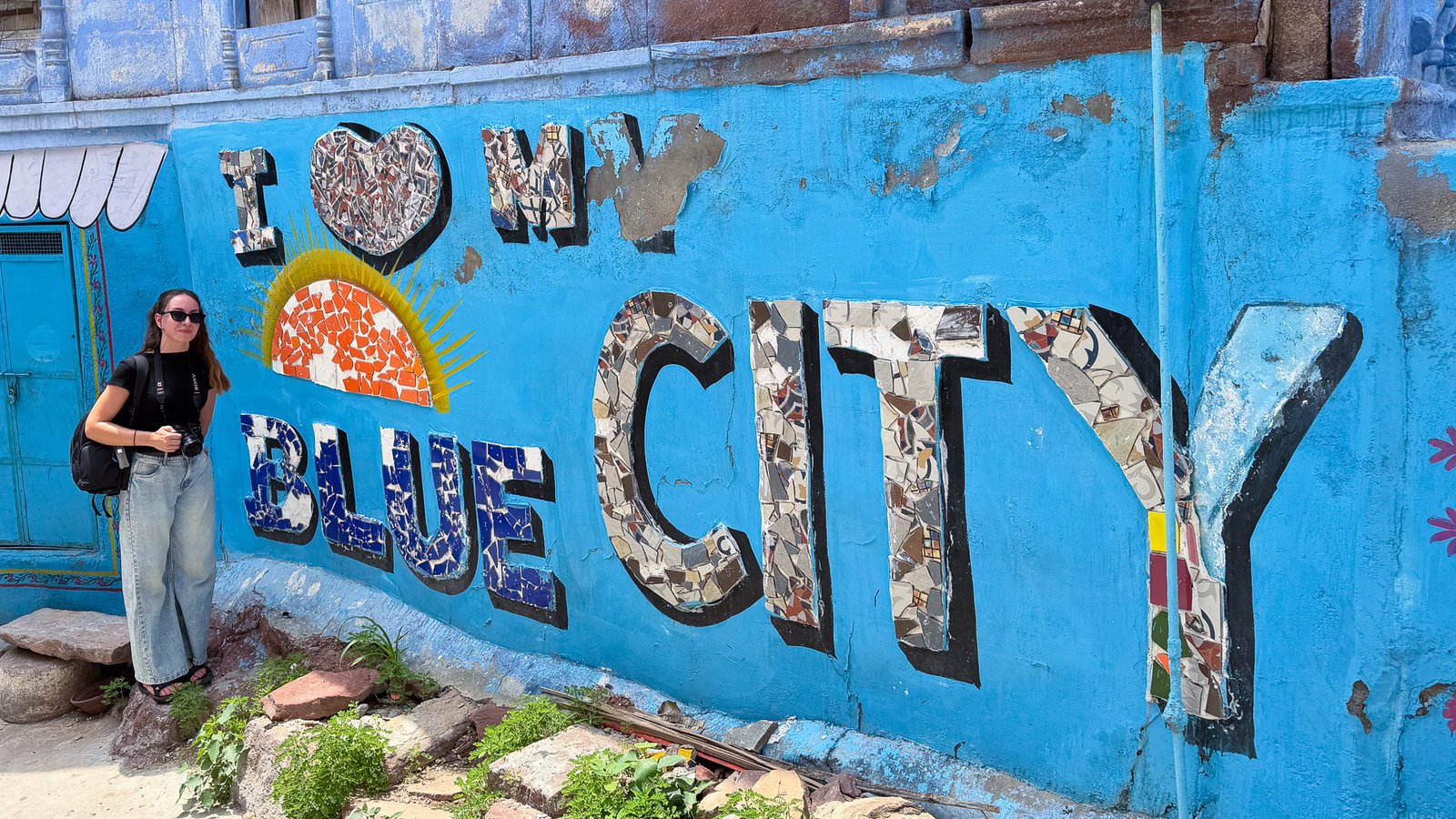 A women stood next to a blue wall that reads "I love my Blue City" in Jodhpur, India