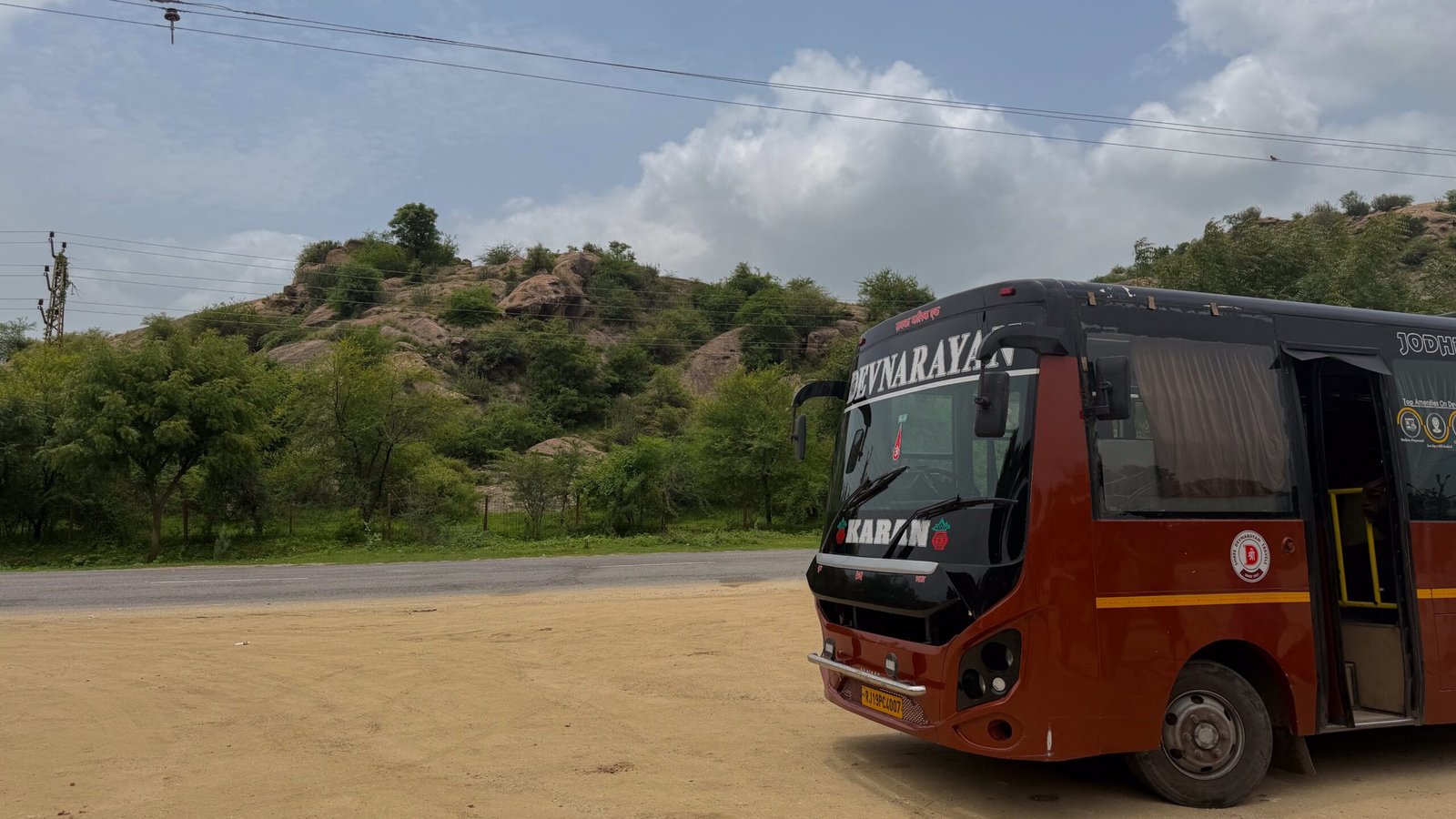 A bus stopped at the side of the road with sandy landscapes in Rajasthan.