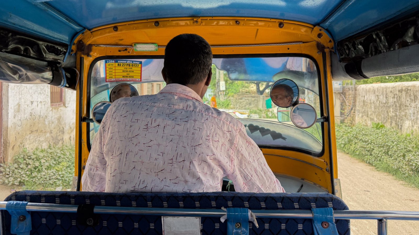 A man driving an auto-rickshaw through backroads.