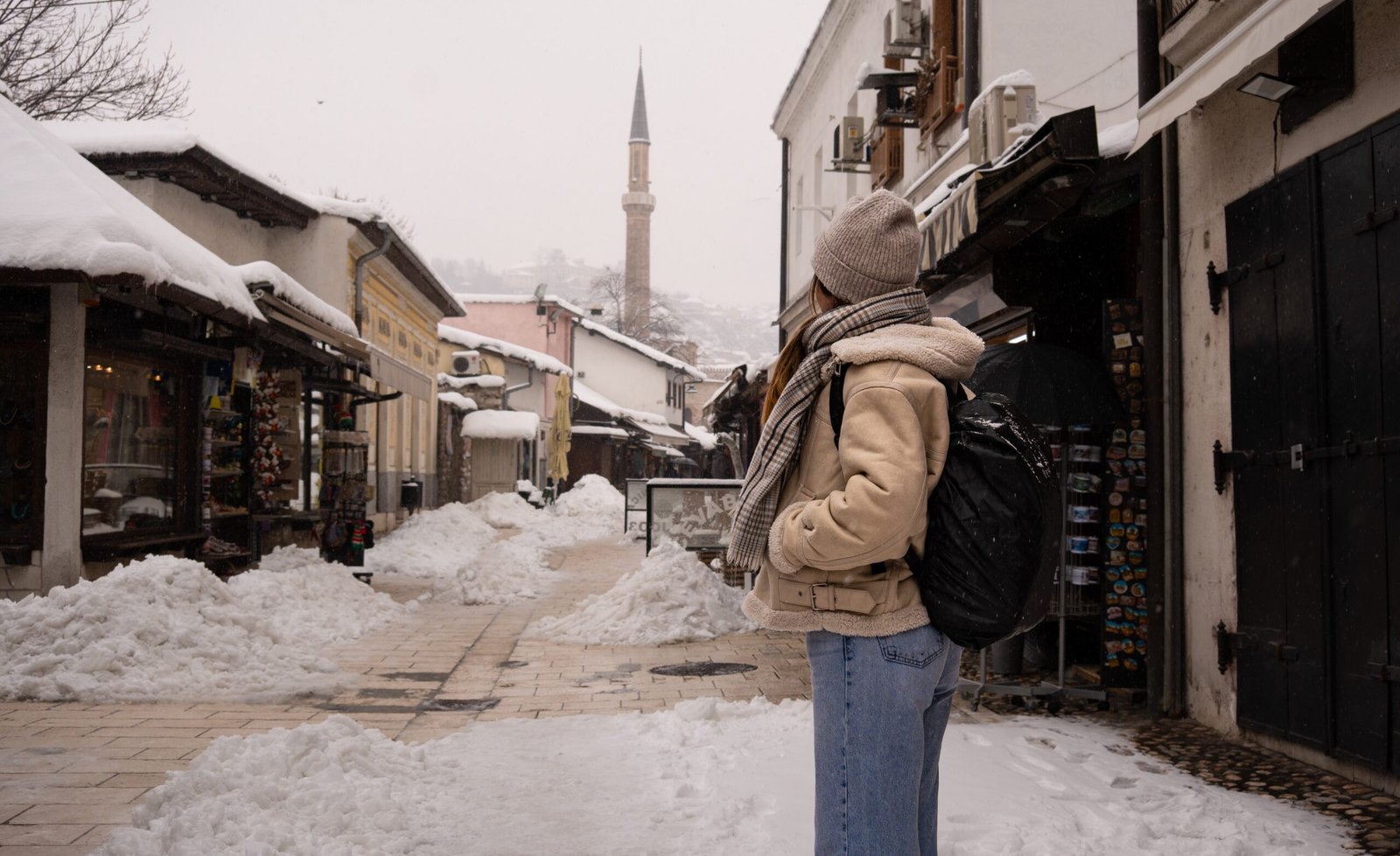 A women stood on a path in a snowy Sarajevo with a minerat in the background